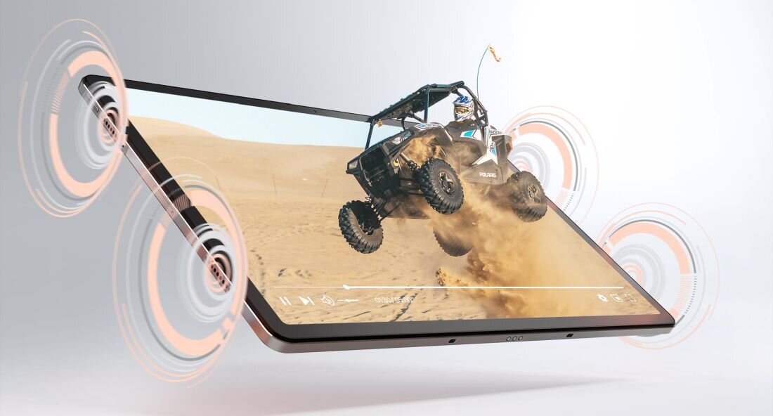 Tablet wyświetla dynamiczną scenę z pojazdem terenowym na pustyni, z widocznymi efektami dźwiękowymi wokół urządzenia. Na ekranie widać pasek odtwarzania multimediów.