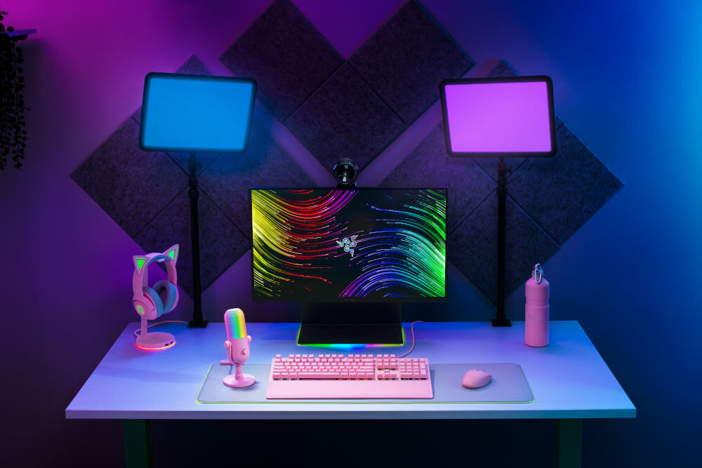 Mikrofon RAZER Seiren V3 Chroma Superkardioidalny Różowy prezentacja mikrofonu na biurku w pokoju gamingowym w tle kolorowe ledy nadające klimatu światła automatyczny limiter wzmocnienia dotykowy czujnik mapowanie poleceń świetna opcja dla graczy