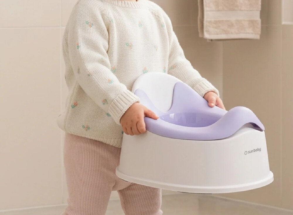 Dziecko trzyma biało-fioletowy nocnik z logo \'sun baby\'.