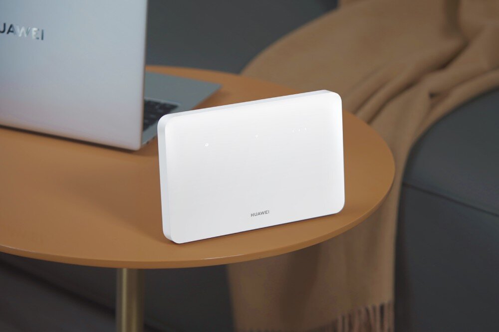 Router HUAWEI 4G CPE 5 B636-336 Biały router Huawei ustawiony na okrągłym brązowym stoliku obok laptopa w jasnym wnętrzu mieszkalnym