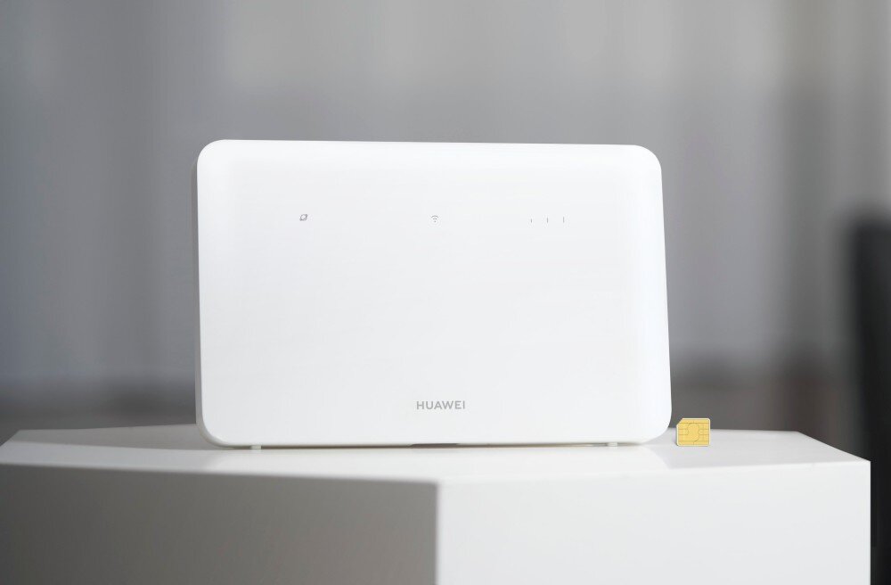 Router HUAWEI 4G CPE 5 B636-336 Biały router Huawei stoi na jasnym podwyższeniu obok złotej karty nano-SIM na rozmytym tle