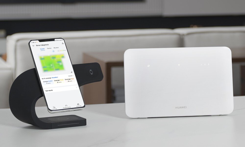 Router HUAWEI 4G CPE 5 B636-336 Biały router Huawei stoi na białym blacie obok smartfona umieszczonego w uchwycie, który wyświetla aplikację z mapą zasięgu Wi-Fi w pomieszczeniach