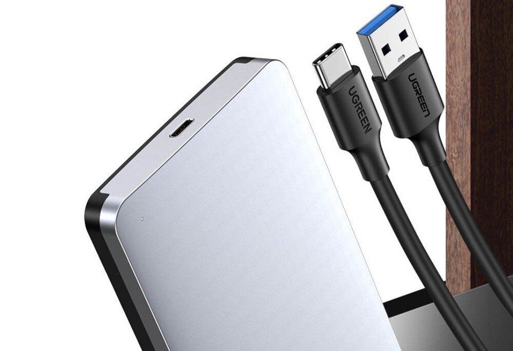 Obudowa dysku UGREEN CM300 Zbliżenie na górną część srebrnej obudowy oraz dwa kable z wtykami USB-C i USB-A. Na czarnych końcówkach kabli widnieje logo marki