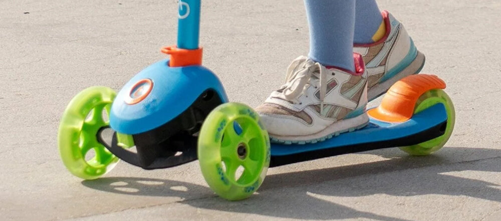 Hulajnoga dla dzieci TRUNKI Mała Niebieski droga dziecko jedzie na hulajnodze zbliżenie na platformę dziecko trzyma stopę na hamulcu tylny hamulec nożny prosta i skuteczna kontrola nad prędkością jazdy lekko nacisnąć hamulec uczy odpowiedzialności i przewidywania szerokie tylne koło stabilizuje tor jazdy