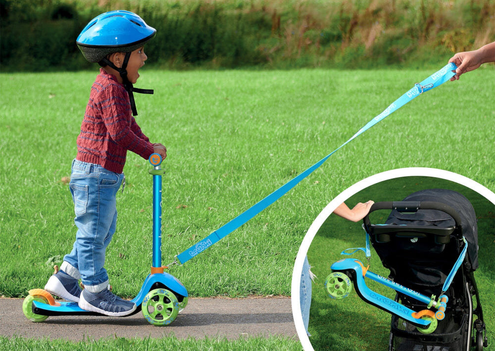 Hulajnoga dla dzieci TRUNKI Mała Niebieski park dziecko na hulajnodze osoba trzyma pasek w dłoni ciągnie za sobą hulajnogę w tle trawnik obok w kółku złożona hulajnoga umieszczona na wózku dziecięcym wspiera rozwój mięśni równowagi koordynacji zdrowe spędzanie czasu na świeżym powietrzu bawi uczy i rozwija bezpieczeństwo i wygodę pasek i torba w zestawie rodzic może przenieść hulajnogę lub ciągnąć dziecko za sobą