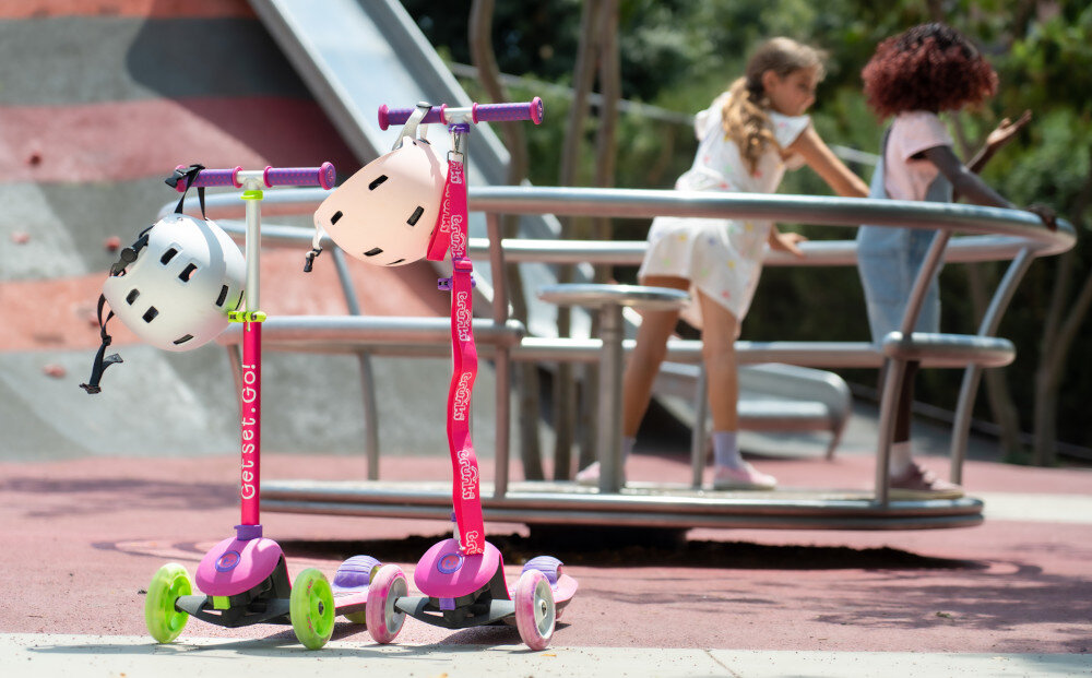 Hulajnoga dla dzieci TRUNKI Mała Różowy park plac zabaw dwie hulajnogi ustawione obok siebie w tle bawi się dwójka dzieci 3 kółka dwa z przodu o średnicy 125 mm jedno z tyłu o średnicy 100 mm pojazd jest stabilny i bezpieczny z połączenia polipropylenu i poliuretanu płynna i stabilna jazda precyzyjne łożyska Spring Steel ogranicza ścieranie