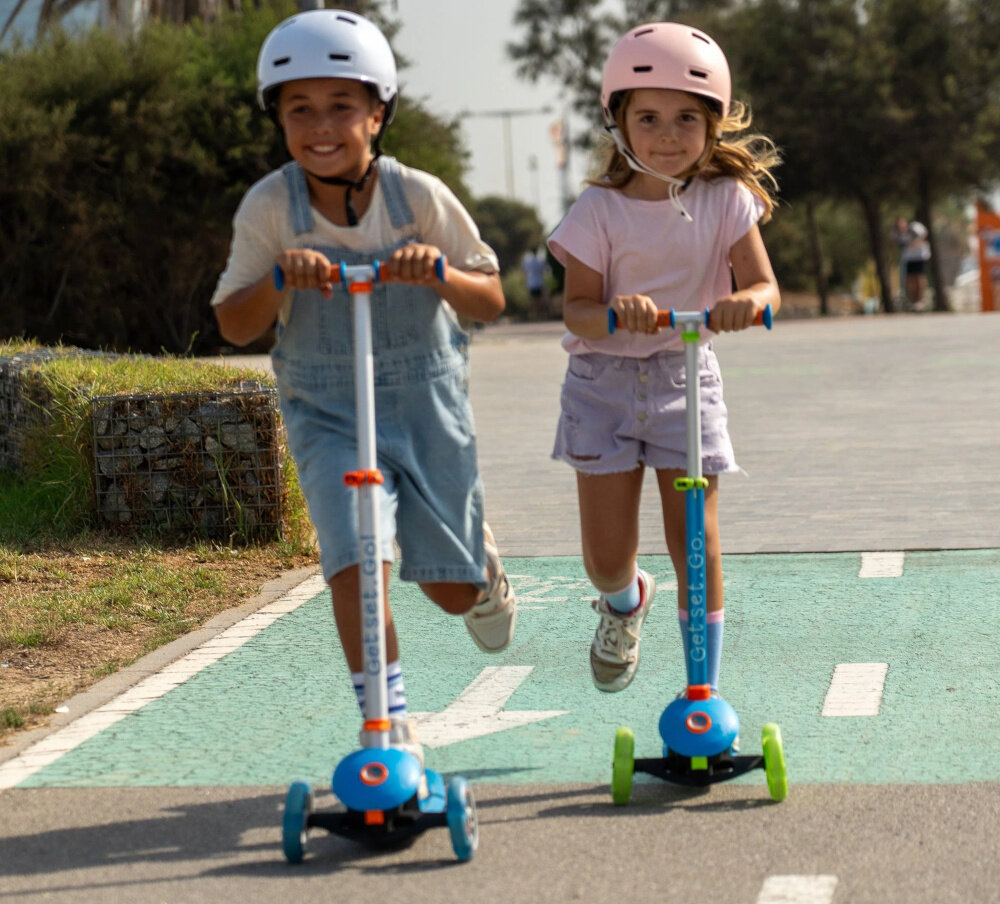 Hulajnoga dla dzieci TRUNKI Duża Niebieski park droga dwójka dzieci jedzie na hulajnogach pod drodze w tle drzewa niebo platforma wykonana z polipropylenu i włókna szklanego solidne podparcie stóp dziecka szerokość 14 cm stabilność odporność na uszkodzenia ułatwia naukę jazd sprzyja nauce równowagi