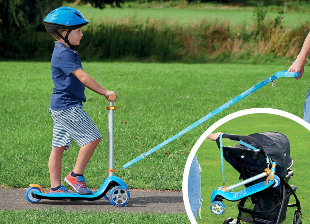 Hulajnoga dla dzieci TRUNKI Duża Niebieski park dziecko na hulajnodze osoba trzyma pasek w dłoni ciągnie za sobą hulajnogę w tle trawnik obok w kółku złożona hulajnoga umieszczona na wózku dziecięcym wspiera rozwój mięśni równowagi koordynacji zdrowe spędzanie czasu na świeżym powietrzu bawi uczy i rozwija bezpieczeństwo i wygodę pasek i torba w zestawie rodzic może przenieść hulajnogę lub ciągnąć dziecko za sobą