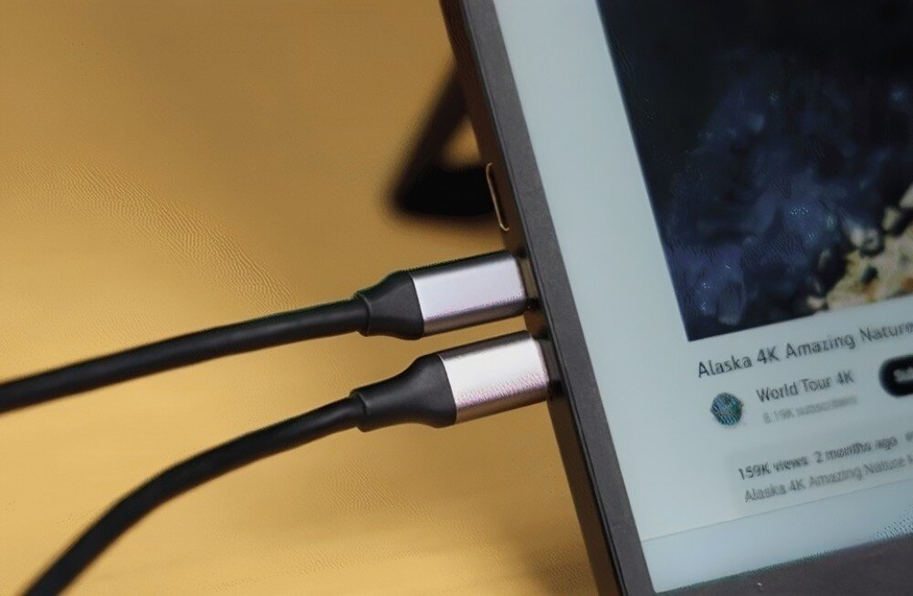 Monitor UPERFECT Ustation Delta Zbliżenie na dwa przewody USB-C podłączone do krawędzi ekranu przenośnego, na wyświetlaczu widać fragment filmu z serwisu wideo, podłączenie, porty, gniazda, kompatybilność