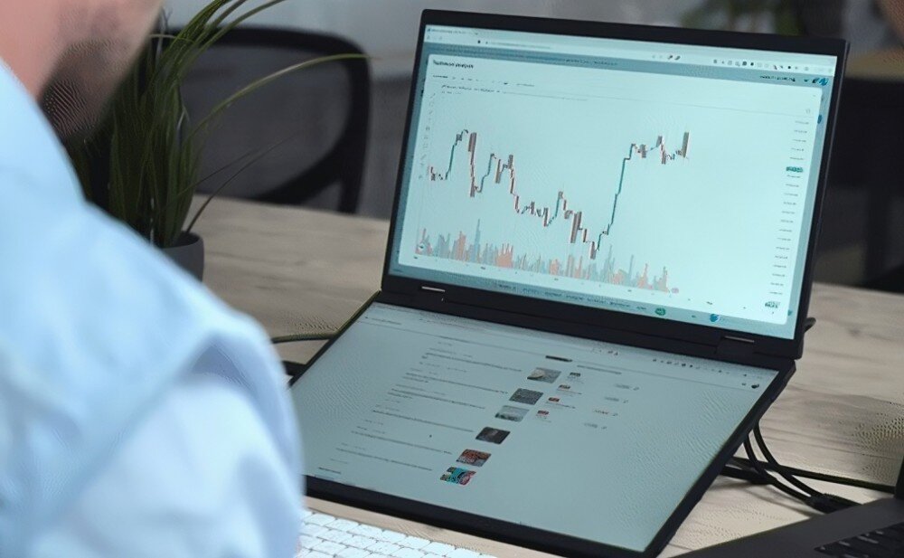 Monitor UPERFECT Ustation Delta Zbliżenie na użytkownika siedzącego przy biurku, który patrzy na dwa pionowo ustawione ekrany z wykresem giełdowym i listą wideo w serwisie internetowym, waga, konstrukcja, grubość