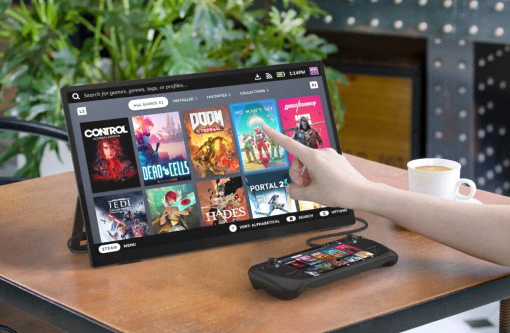 Monitor UPERFECT USteam E6 Pro Ręka dotykająca ekran ustawionego na stole monitora, na którym widać bibliotekę gier z kolorowymi okładkami, obok leży konsola i stoi filiżanka kawy, przekątna, rozdzielczość, obsługa dotykowa