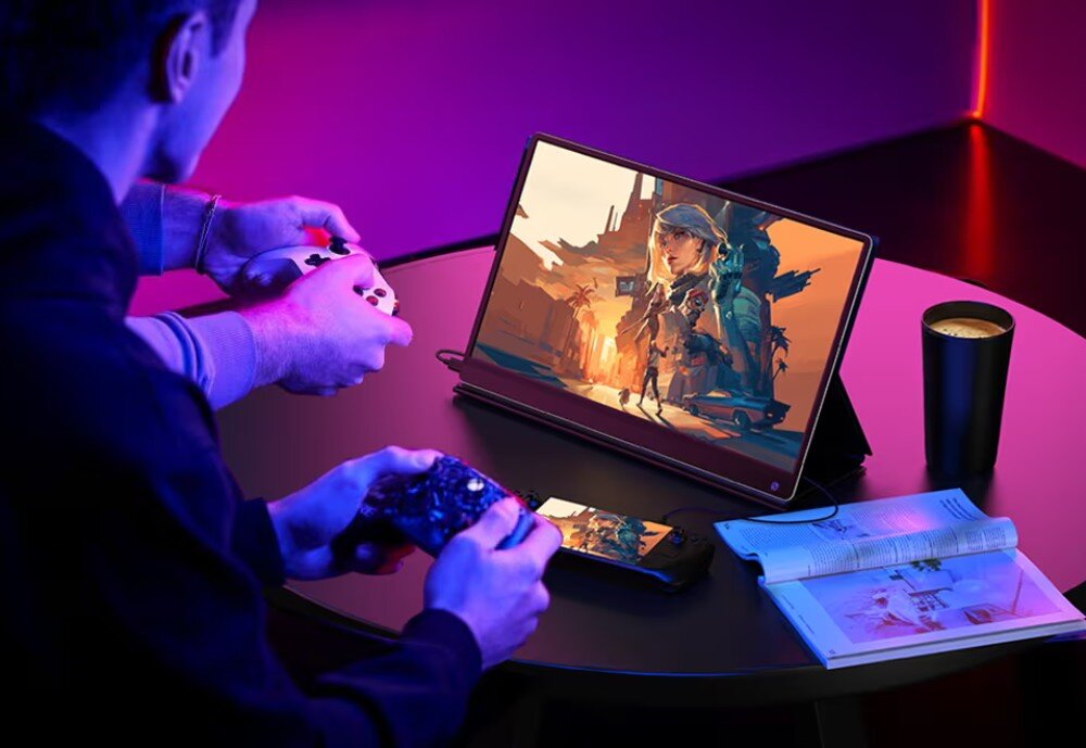 Monitor UPERFECT USteam G16 Dwóch graczy siedzących przy okrągłym stoliku, każdy trzyma kontroler, przed nimi monitor z wyświetlaną grą i konsola przenośna leżąca na blacie, opis