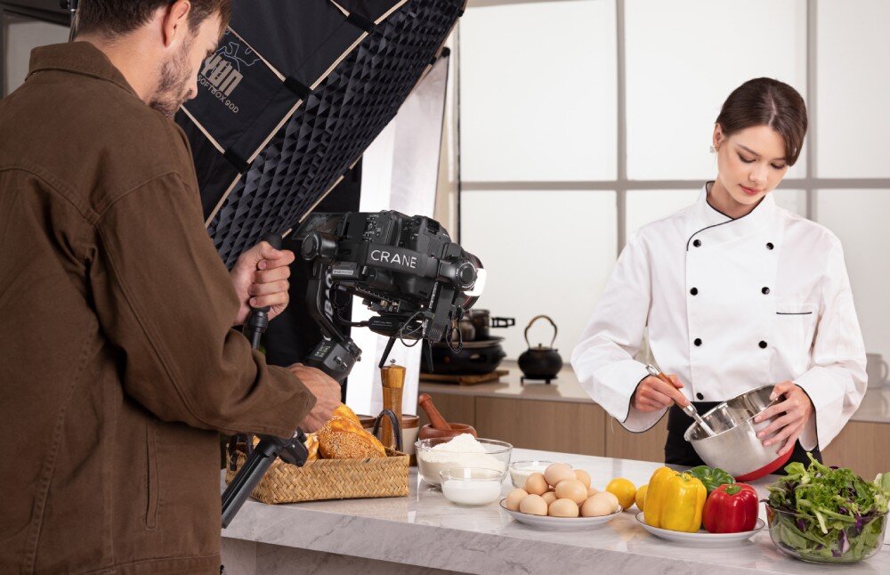 Gimbal ZHIYUN Crane 4 Combo Mężczyzna w brązowej kurtce rejestruje materiał w kuchni, trzymając aparat na stabilizatorze, kalibracja, wyważenie, wskaźnik