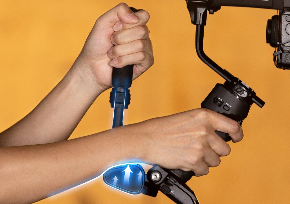 Gimbal ZHIYUN Crane 4 Combo Ręce trzymające uchwyt stabilizatora, na którym zaznaczono kierunek regulacji. Dłoń obejmuje dodatkowy uchwyt, uchwyty, regulacja, otwory montażowe