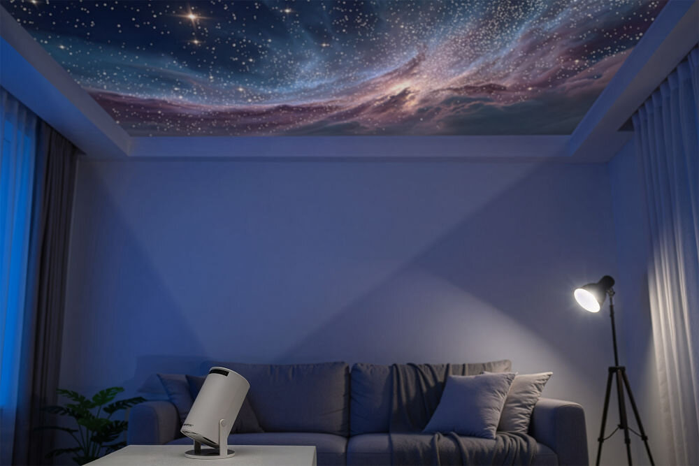 Projektor WANDOO LMP360 HD (1280 x 720), 160 ANSI lumen, Wi-Fi, Bluetooth Salon z sofą i lampą podłogową w półmroku, gdzie z małego projektora Wandoo na stoliku kawowym wyświetlana jest na suficie dynamiczna projekcja rozgwieżdżonej mgławicy. Projektor Wandoo wyświetlający galaktykę na suficie w salonie.