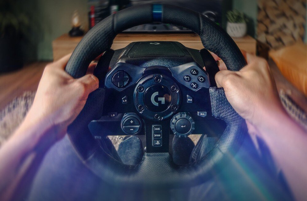 Kierownica LOGITECH G923 + Shifter Bundle Widok z perspektywy pierwszej osoby na dłonie trzymające skórzaną kierownicę wyścigową z wbudowanym panelem przycisków