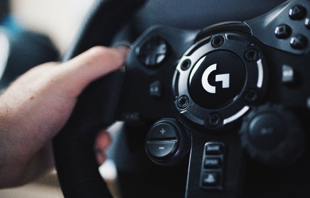 Kierownica LOGITECH G923 + Shifter Bundle Zbliżenie na środkową część kierownicy wyścigowej z logo oraz dłoń spoczywającą na jej obrzeżu