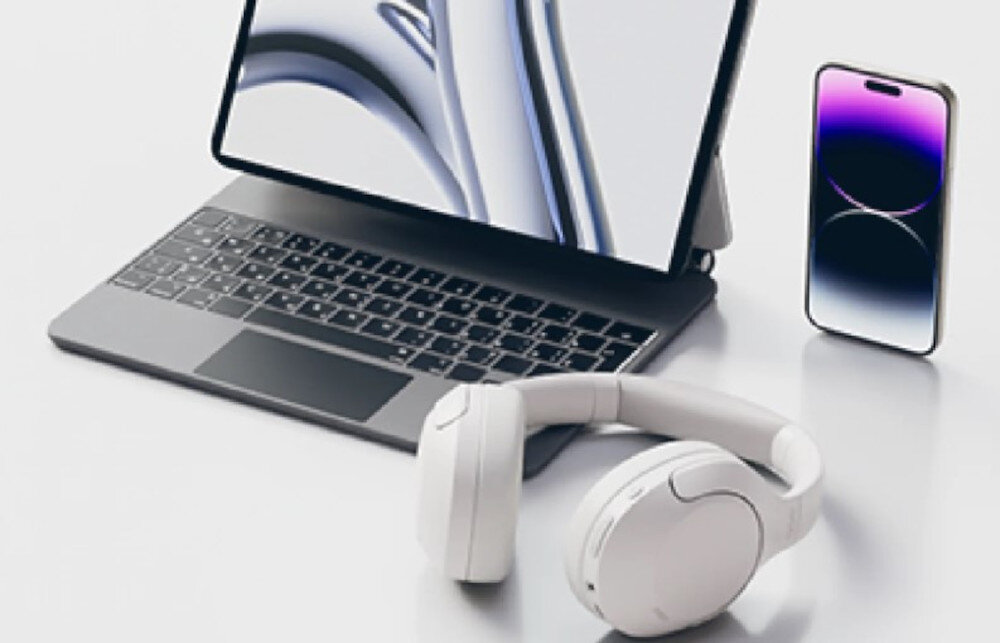 Słuchawki nauszne QCY H3 Lite multipoint połączenie dwóch urządzeń jednocześnie, słuchawki nauszne leżące na białym blacie, smartfon oraz laptop