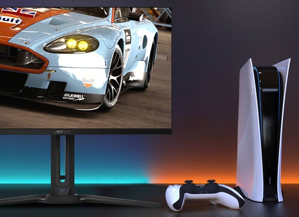 Monitor GIGABYTE Aorus FO27Q2 Konsola PlayStation 5 i pad stoją obok monitora wyświetlającego wyścigówkę. Pod ekranem widoczny jest subtelny pasek podświetlenia RGB, kompatybilność, konsole