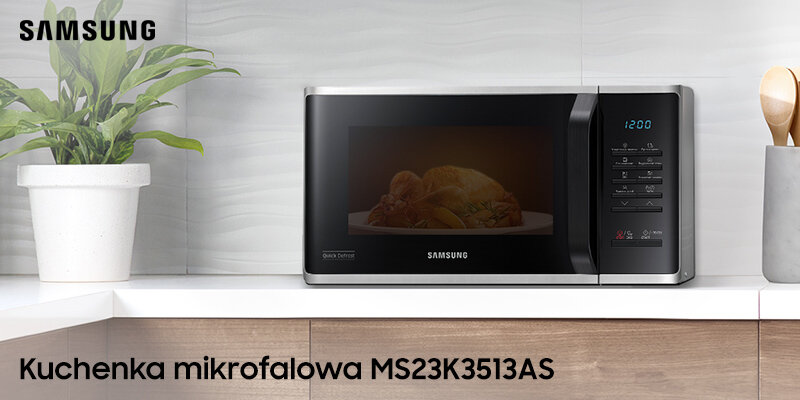 Kuchenka mikrofalowa Samsung z wyświetlaczem cyfrowym i przyciskami dotykowymi, obok roślina w doniczce i drewniana łyżka. Widoczny tekst: \'Kuchenka mikrofalowa MS23K3513AS\'.