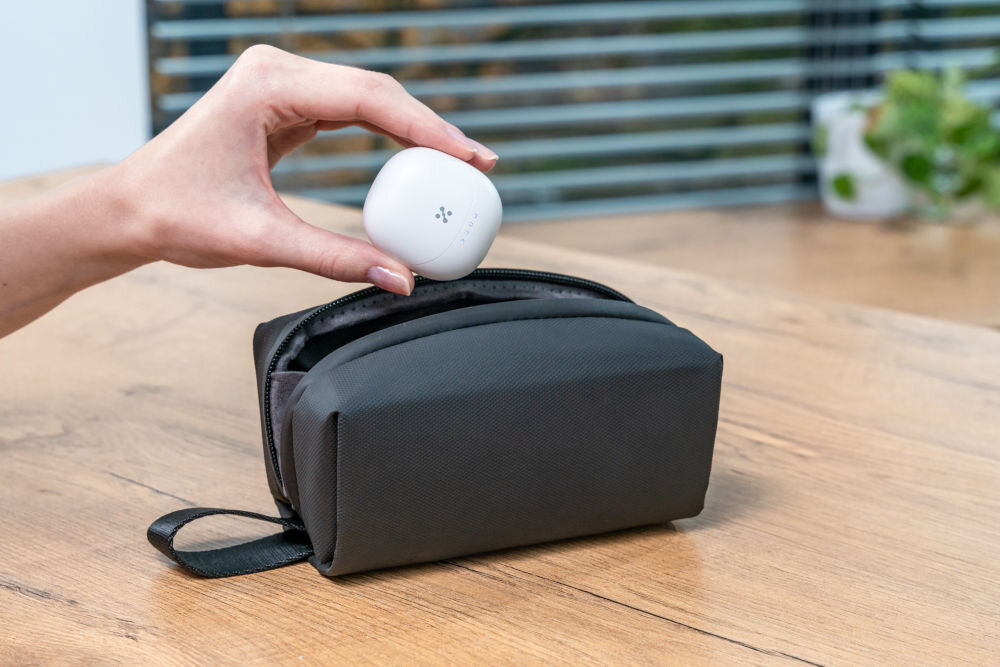 Słuchawki douszne XMUSIC XTW300W biały Dłoń trzyma zamknięte, czarne etui do słuchawek z widocznym logo i diodami, unosząc je nad otwartym, czarnym pokrowcem materiałowym (saszetką).