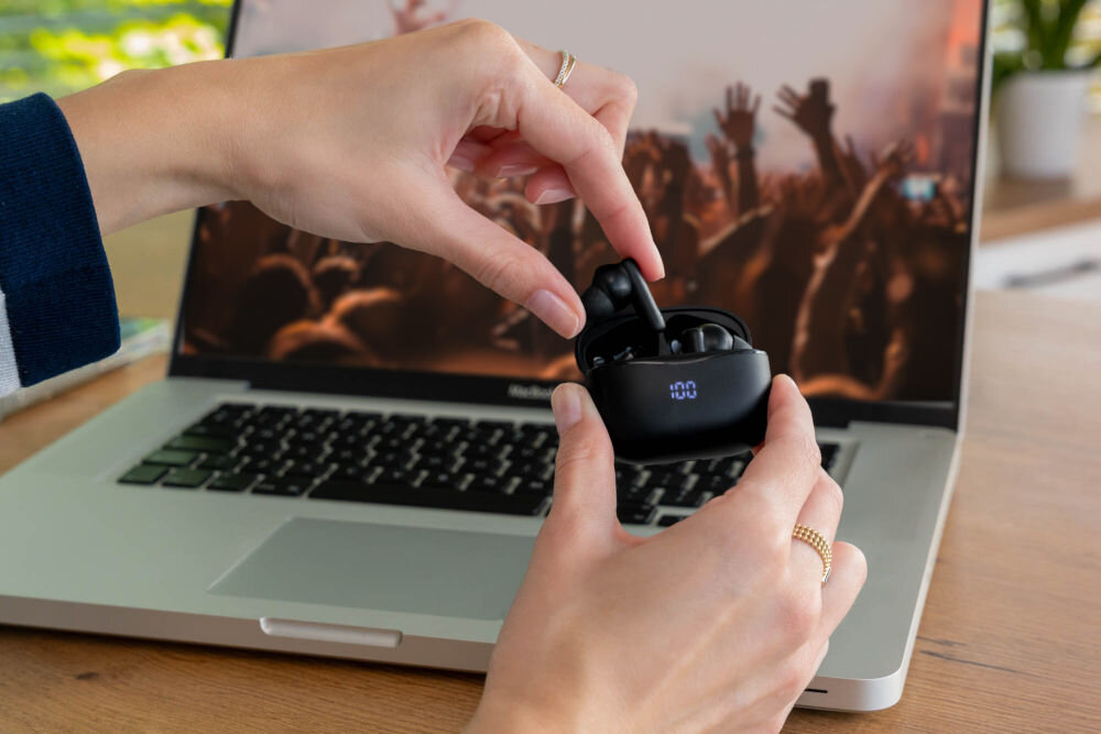 Słuchawki dokanałowe XMUSIC XTW500K Kobieta wyjmuje czarną słuchawkę bezprzewodową XMUSIC XTW500K z etui ładującego z wyświetlaczem LED.