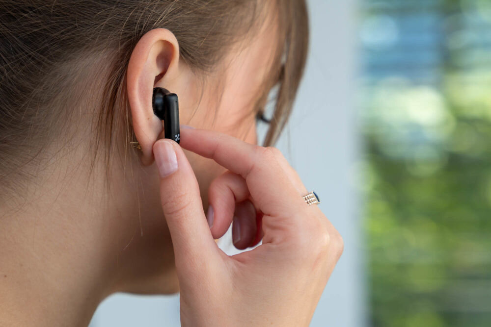 Słuchawki dokanałowe XMUSIC XTW500K Kobieta dotyka panelu sterowania na słuchawce XMUSIC XTW500K, prezentując funkcję obsługi dotykowej.