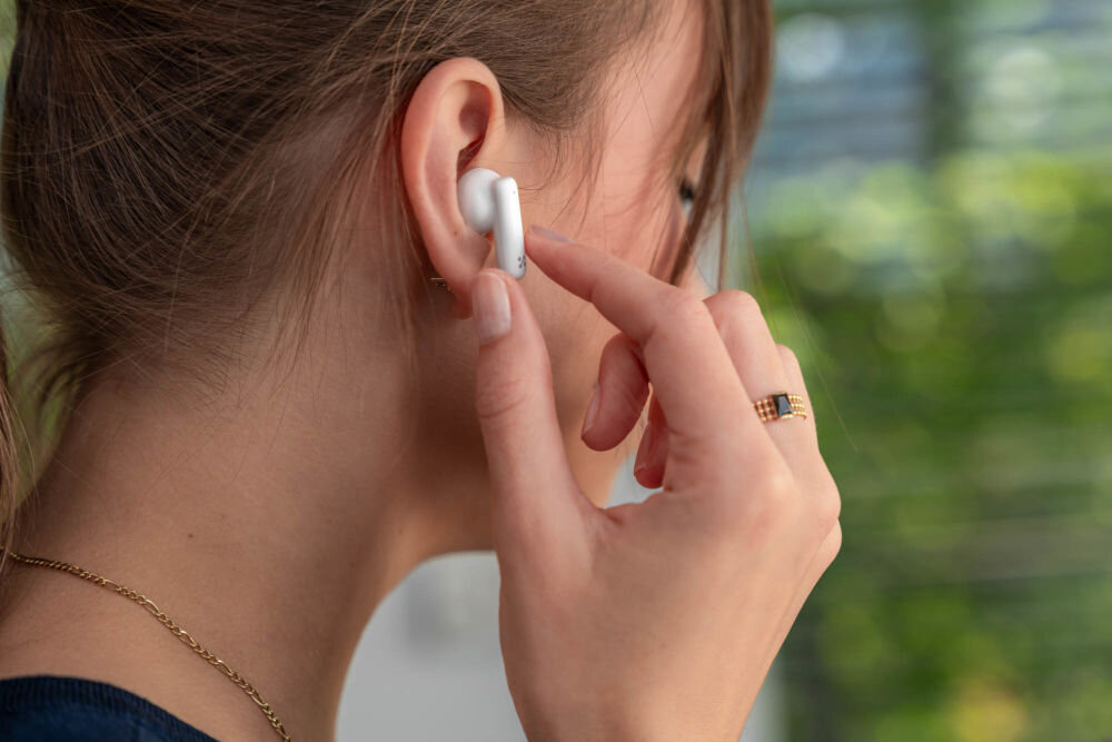 Słuchawki dokanałowe XMUSIC XTW500W Kobieta dotyka panelu sterowania na słuchawce XMUSIC XTW500W, prezentując funkcję obsługi dotykowej.