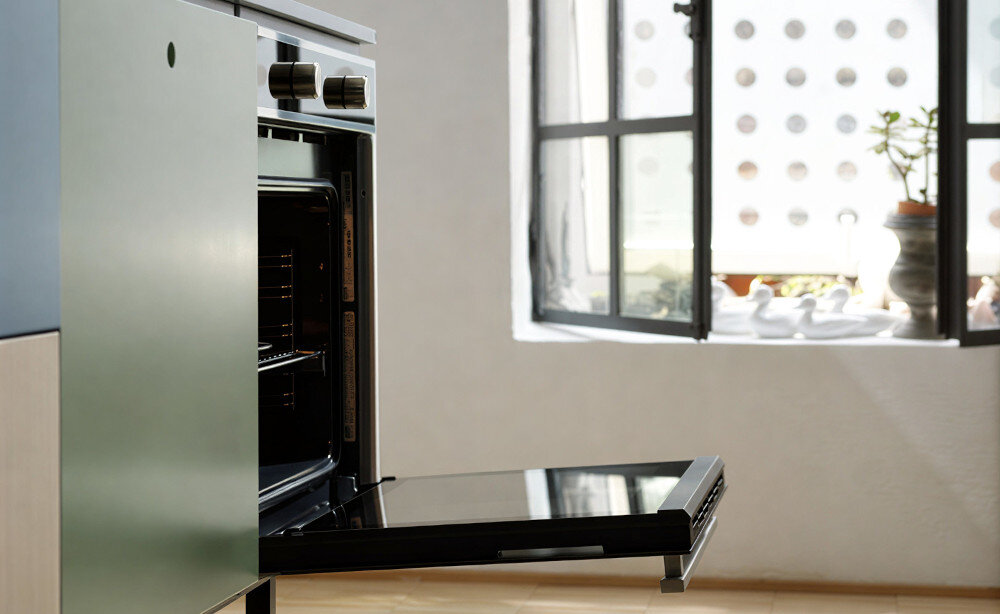 Piekarnik FRANKE Smart FSM 86 H XS Widok z boku pokazuje piekarnik z uchylonymi drzwiczkami w stylowej kuchni. W tle widoczne jest duże okno doświetlające pomieszczenie
