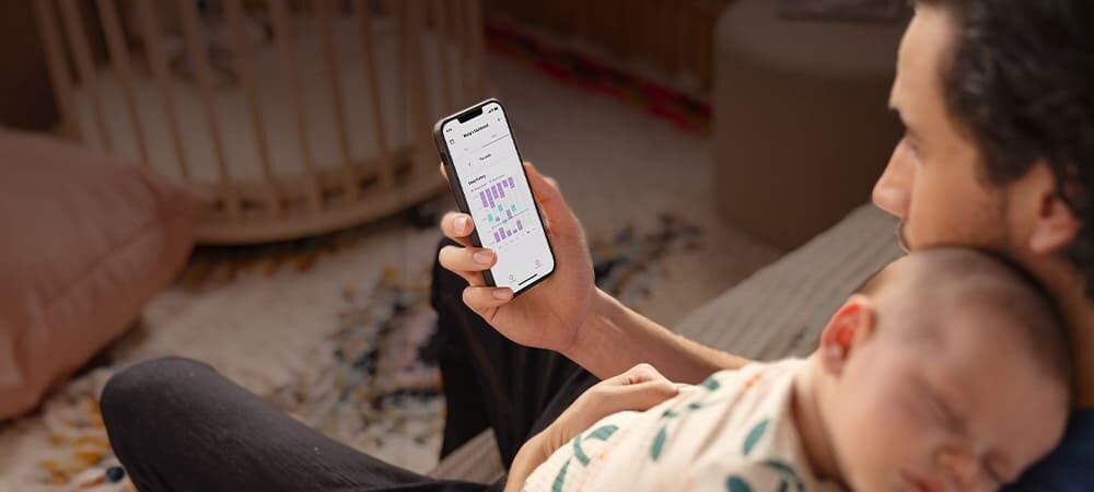 Mężczyzna ze śpiącym niemowlęciem, trzymający w dłoni telefon z aplikacją Baby Monitor+