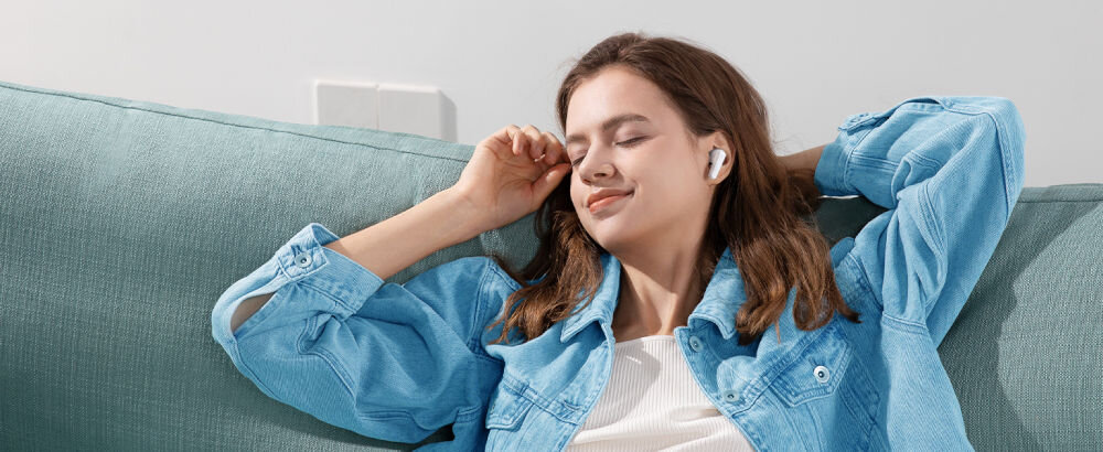 Słuchawki dokanałowe SOUNDCORE R50i v2 biały szum relaks skupienie sen aplikacja, osoba z założonymi słuchawkami dokanałowymi siedząca na kanapie