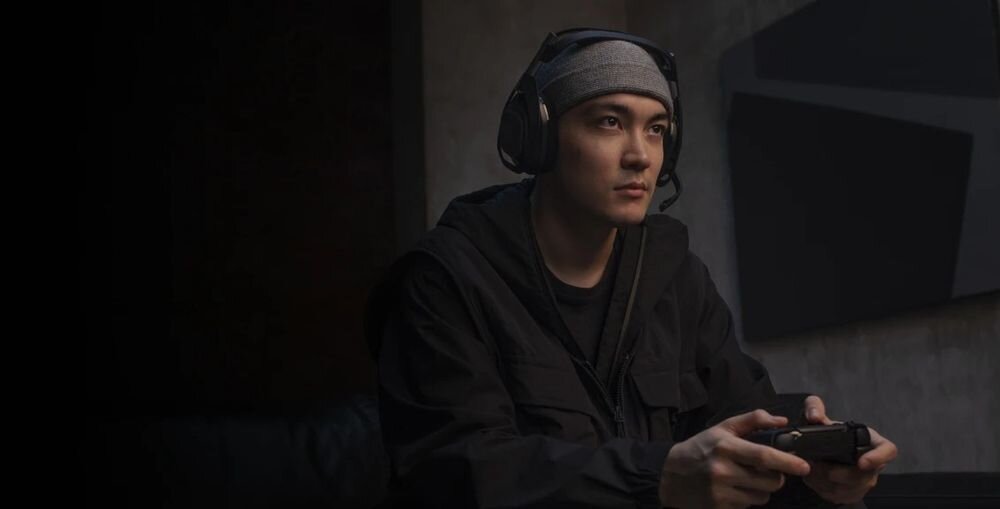 Słuchawki LOGITECH Astro A50 (Gen 5) Bluetooth miksowanie dźwięku Discord urządzenie mobilne, osoba z założonymi słuchawkami gamingowymi trzymająca kontroler w ręku