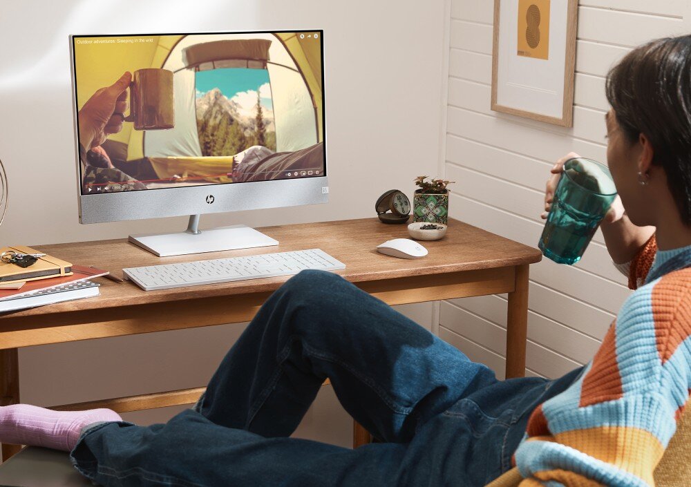 Komputer HP Pavilion 27-ca2092nw Osoba siedzi z kubkiem przy biurku i ogląda film z widokiem na góry i namiot na ekranie komputera typu all-in-one, matowa powłoka, ochrona wzroku