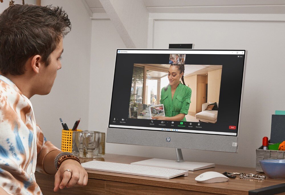 Komputer HP Pavilion 27-ca2092nw Osoba prowadzi wideorozmowę przez aplikację, patrząc na ekran komputera typu all-in-one, na którym widać rozmówczynię w zielonej koszuli, kamera internetowa, mikrofon, audio