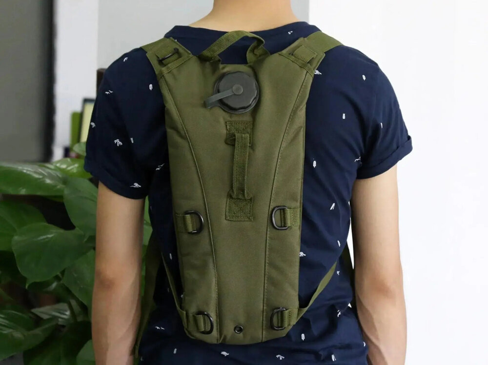 Plecak EXTRALINK Hydracyjny MIL-1114 Zielony pomieszczenie osoba stoi tyłem ma plecak na plecach widok od przodu w tle ściana i kwiaty na każdą okazję stały dostęp do wody bezpieczeństwo wygoda