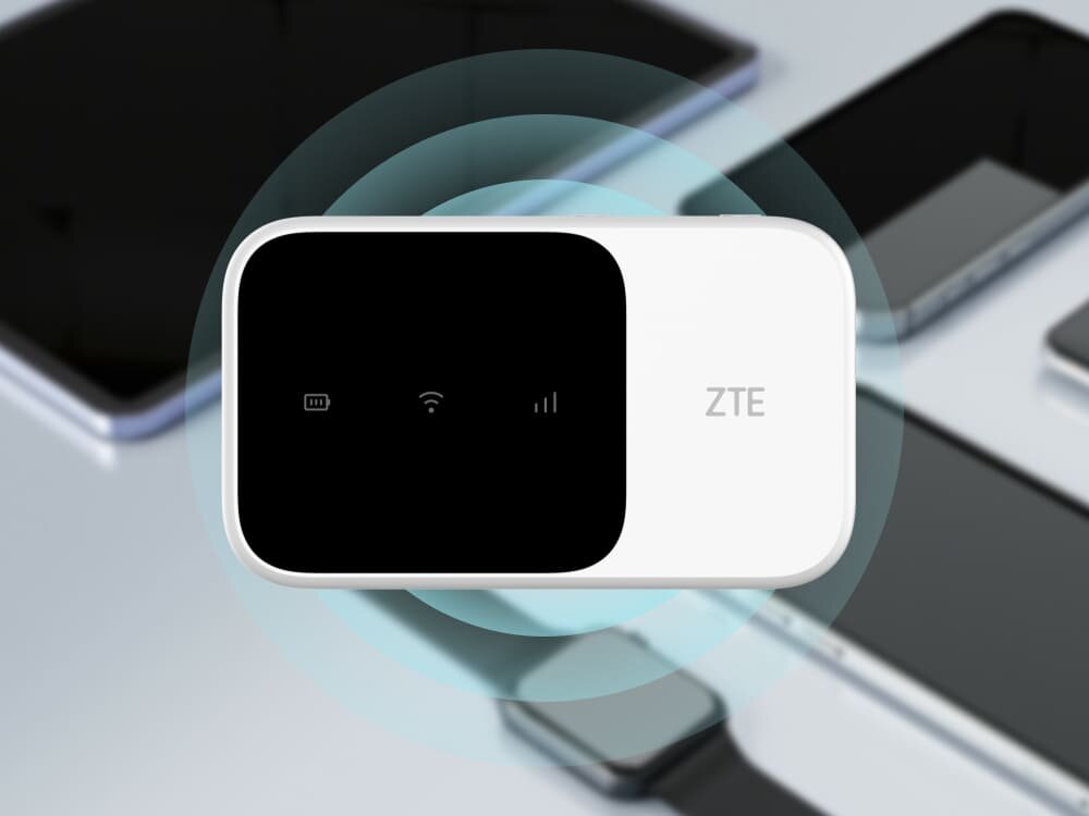 Router ZTE MF986C 4G LTE Białe mobilne urządzenie Wi-Fi ZTE z czarnym ekranem wyświetlającym ikony baterii, Wi-Fi i sygnału. W tle rozmyte urządzenia technologiczne, co podkreśla wygodny dostęp do internetu w każdej sytuacji, 