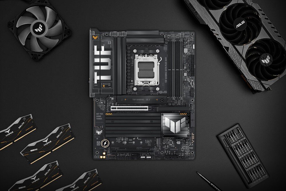 Płyta główna ASUS TUF Gaming X870-Plus WiFi Płyta główna ułożona na płaskiej powierzchni w otoczeniu karty graficznej kości pamięci RAM wentylatora i zestawu narzędzi