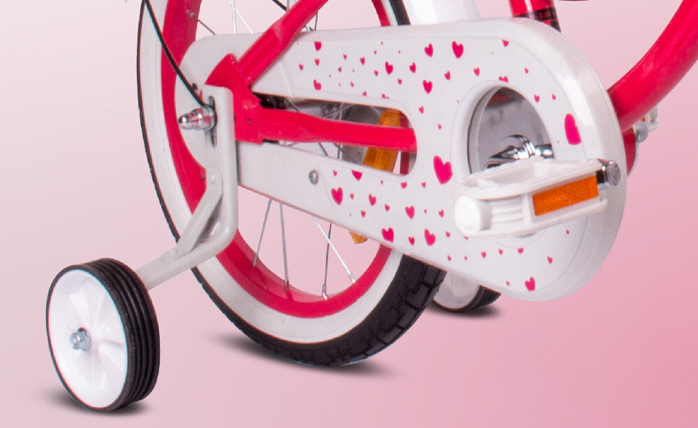 Rower dziecięcy SUN BABY Heart bike 16 cali dla dziewczynki Malinowy zbliżenie na kółka boczne i osłonę łańcucha zdjęcie na różowym tle boczne kółka asekurują dziecko w początkowej fazie nauki boczne kółka można łatwo usunąć osłona łańcucha grafika w serduszka zabezpiecza łańcuch przed brudem
