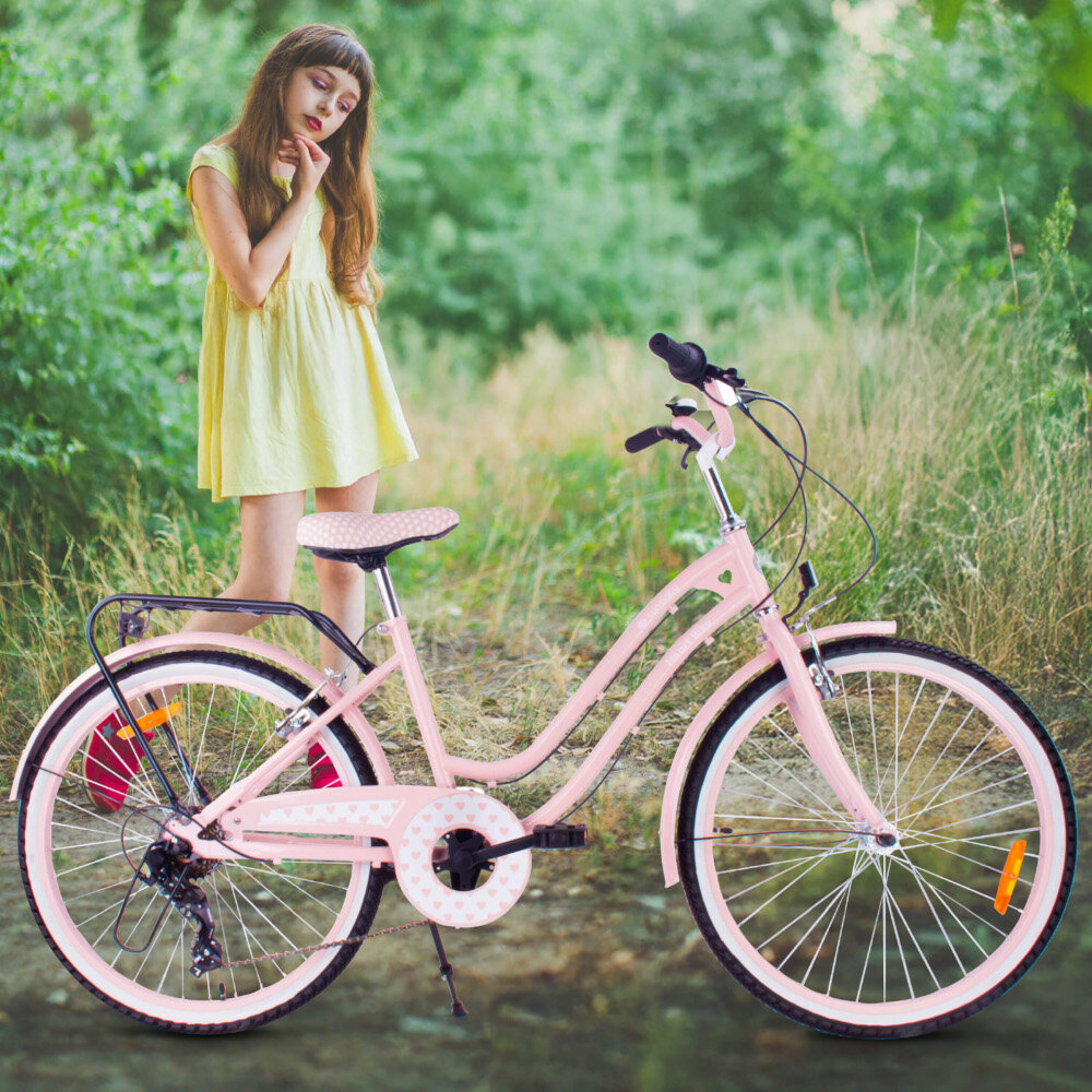 Rower młodzieżowy SUN BABY Heart Bike 24 cale dla dziewczynki Różowy rower na trawie oparty o stopkę w tle dziewczynka na łące stopka w centralnym punkcie ciężkości reflektory odblaskowe z przodu z tyłu i na szprychach roweru lepsza widoczność na drodze bezpieczeństwo dzwonek