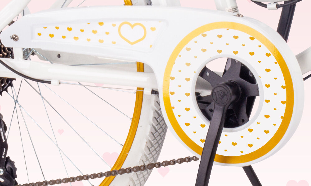 Rower młodzieżowy SUN BABY Heart Bike 24 cale dla dziewczynki Biało-złoty zbliżenie na osłonę łańcucha zdjęcie na jasnym tle osłona łańcucha grafika w serduszka zabezpiecza łańcuch przed brudem błotniki elegancki wygląd osłaniają odzież