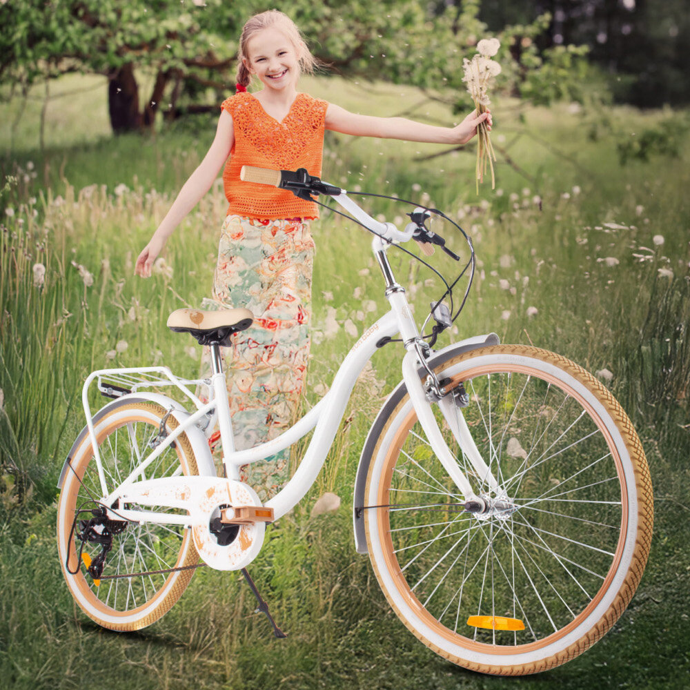 Rower młodzieżowy SUN BABY Flower Bike 24 cale dla dziewczynki Biało-beżowy rower na trawie oparty o stopkę w tle dziewczynka na łące stopka w centralnym punkcie ciężkości reflektory odblaskowe z przodu z tyłu i na szprychach roweru lepsza widoczność na drodze bezpieczeństwo dzwonek