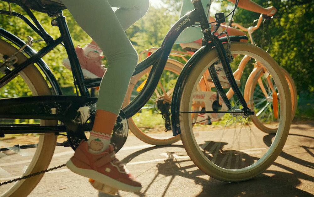 Rower młodzieżowy SUN BABY Flower Bike 24 cale dla dziewczynki Czarny dwoje dzieci jedzie na rowerach po drodze rowerowej w tle trawa i drzewa zbliżenie na koła 24-calowe koła szeroki opony marki RALSON aluminiowe obręcze stabilne trzymanie opony bezpieczna jazda regularne sprawdzanie ciśnienia powietrza wartość na bocznej części opony