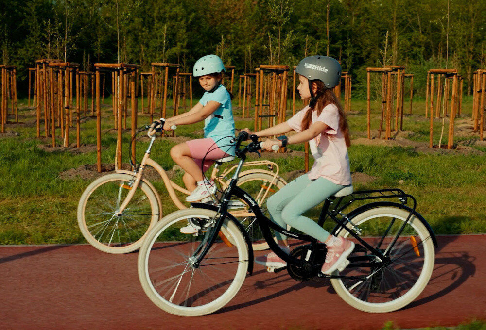 Rower młodzieżowy SUN BABY Flower Bike 24 cale dla dziewczynki Czarny chodnik w parku dwoje dzieci jedzie na rowerach po drodze rowerowej w tle trawa i drzewa 7 biegów obrotowa manetka Revoshift tylna przerzutka SHIMANO Tourney przerzutki SHIMANO duża wytrzymałość sprawne działanie płynna bezproblemowa zmiana biegów