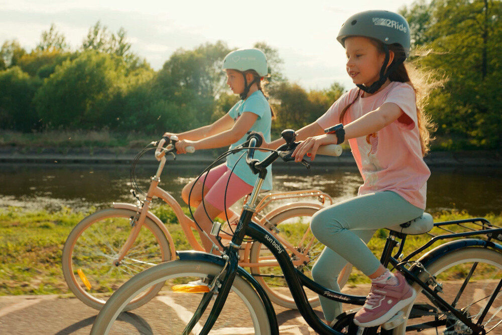 Rower młodzieżowy SUN BABY Flower Bike 24 cale dla dziewczynki Czarny dwoje dzieci jedzie na rowerach po drodze rowerowej w tle trawa i drzewa bezpieczna satysfakcjonująca aktywność wygodne siodełko regulacja w zakresie od 71 do 87 cm