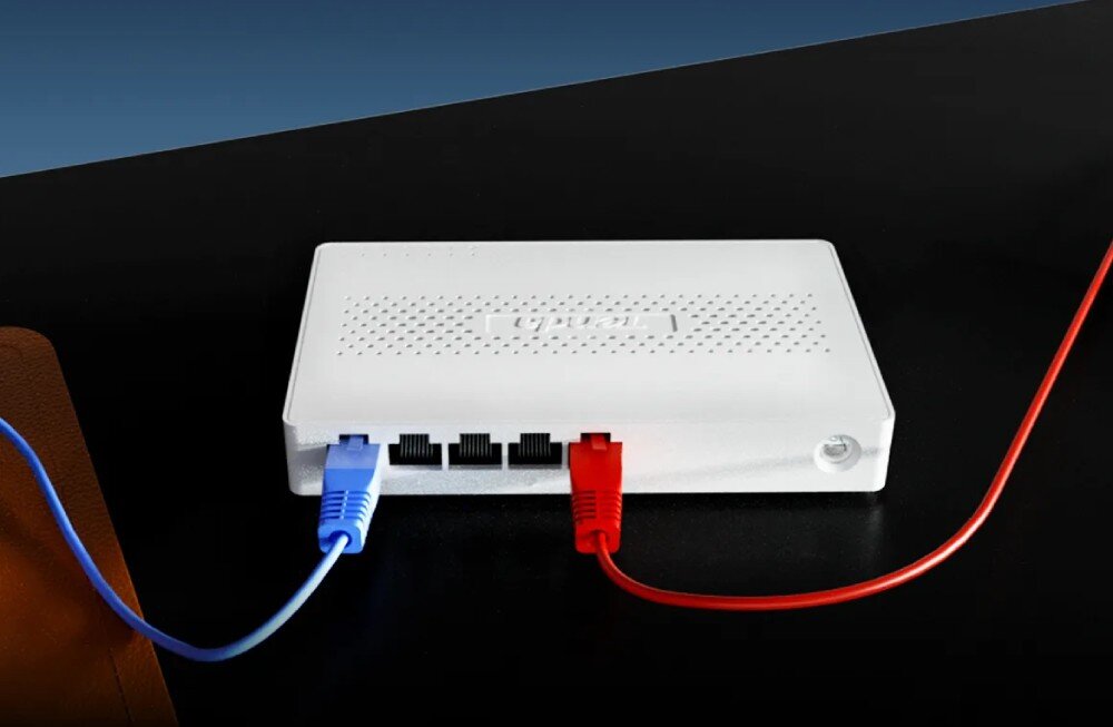 Switch TENDA SM105 Urządzenie sieciowe leżące na płaskiej powierzchni, do którego podłączone są dwa kable: jeden z lewej i jeden z prawej strony, konstrukcja, działanie, funkcje