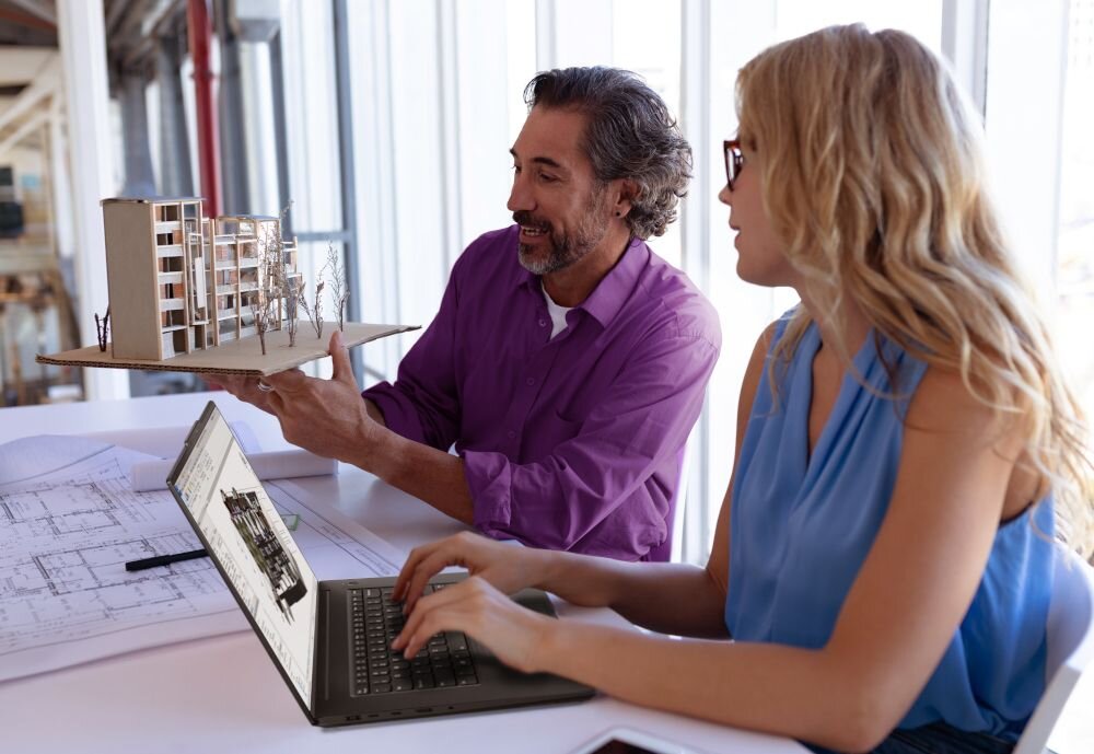 Dwoje architektów analizujących projekt budynku na laptopie Lenovo ThinkPad przy makiecie architektonicznej w jasnym biurze - wymienna pamięć LPCAMM