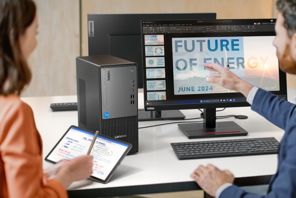 Komputer LENOVO ThinkCentre neo 50t Gen 5 Stanowisko biurowe z pionową obudową komputerową stojącą na białym blacie obok monitora, na którym wyświetlana jest prezentacja z napisem 'FUTURE OF ENERGY', oraz dwiema osobami omawiającymi zawartość ekranu, opis