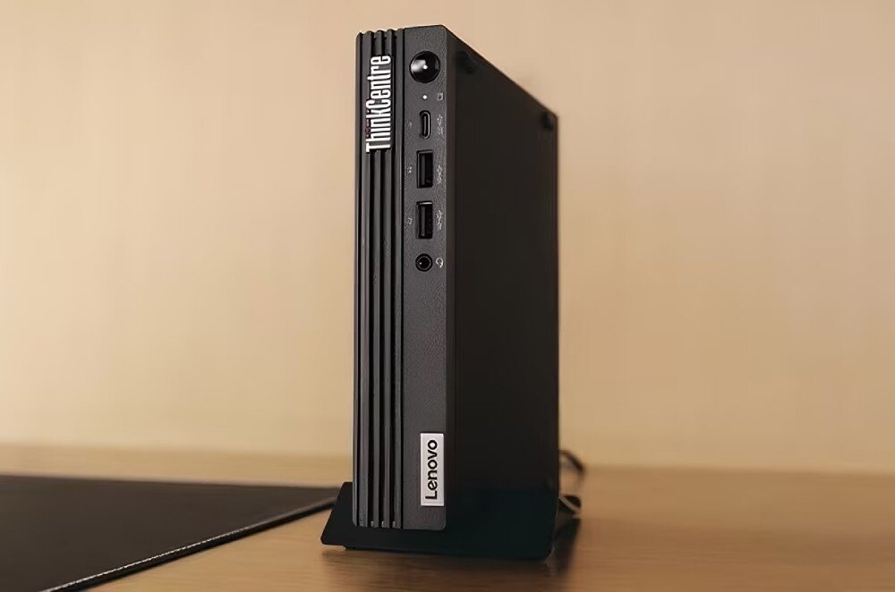 Komputer LENOVO ThinkCentre M75q Gen 5 Komputer w formacie mini ustawiony pionowo na podstawce, widoczne przednie porty i logo z napisem 'ThinkCentre', opis