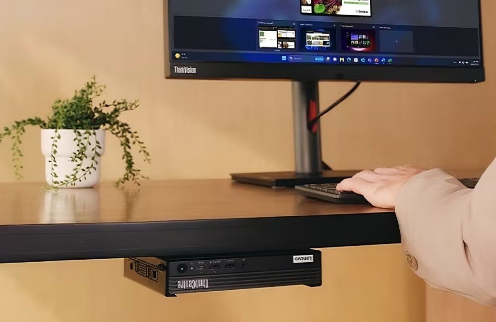 Komputer LENOVO ThinkCentre M75q Gen 5 Mały komputer przymocowany pod biurkiem z monitorem, klawiaturą i ręką osoby obsługującej komputer, wielkość, obudowa, organizacja przestrzeni