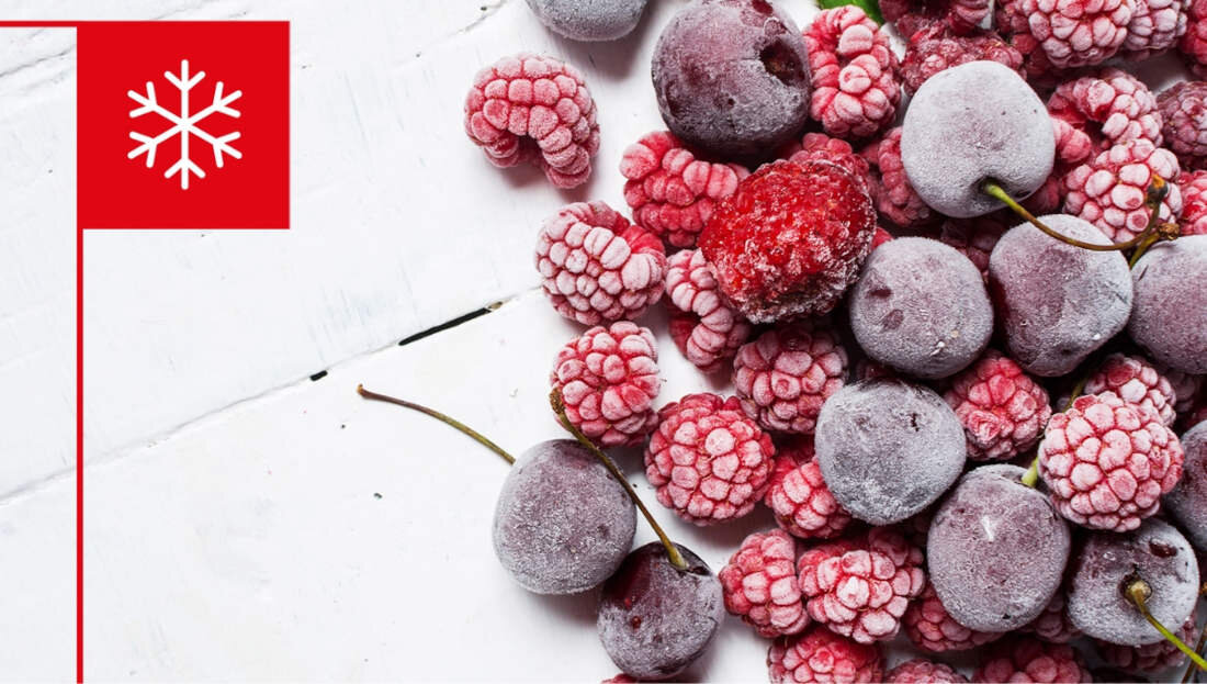 Na obrazie widoczne są zamrożone owoce, takie jak wiśnie i maliny, ułożone na białym tle. W lewym górnym rogu znajduje się czerwony kwadrat z białym symbolem płatka śniegu.